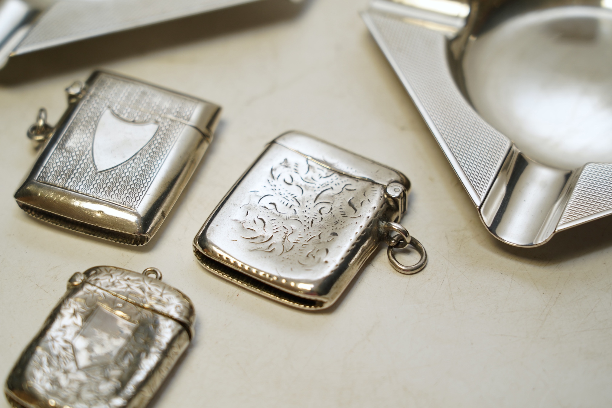 A pair of George V Asprey & Co silver ashtrays, 86mm and three assorted silver vesta cases. Condition - fair to poor.